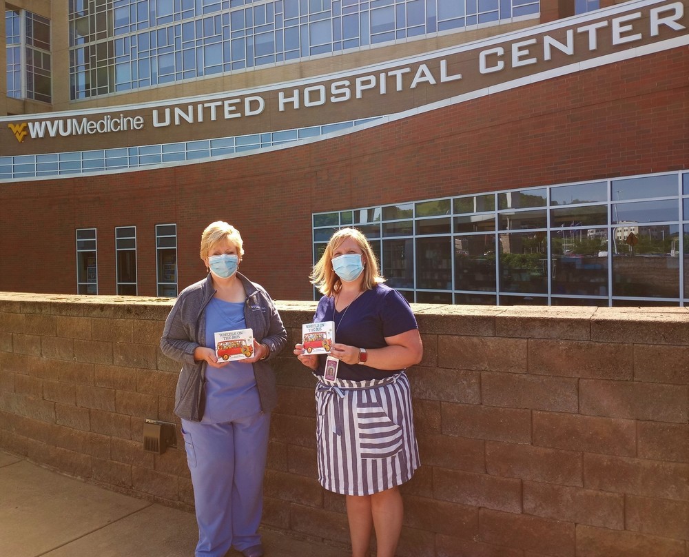 Lee Ann Romeo, RNC, CCE, CLC, Childbirth Educator and Lactation Counselor/Supervisor at UHC accepting multiple copies of the book—“The Wheels on the Bus” from Helen Roberts, NBCT, Federal Programs Curriculum Coordinator for Harrison County Schools